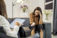 Woman struggling with schizophrenia holds a hand to her head while speaking to an unseen therapist.