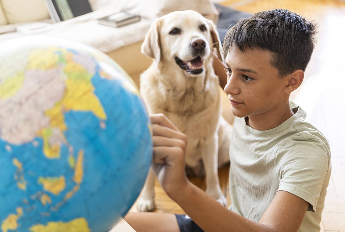 Boy observes a globe and pets a dog