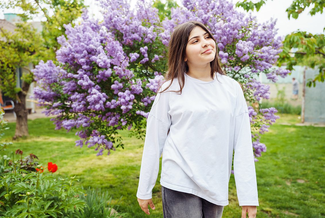 Teen girl in white sweater walks in a garden